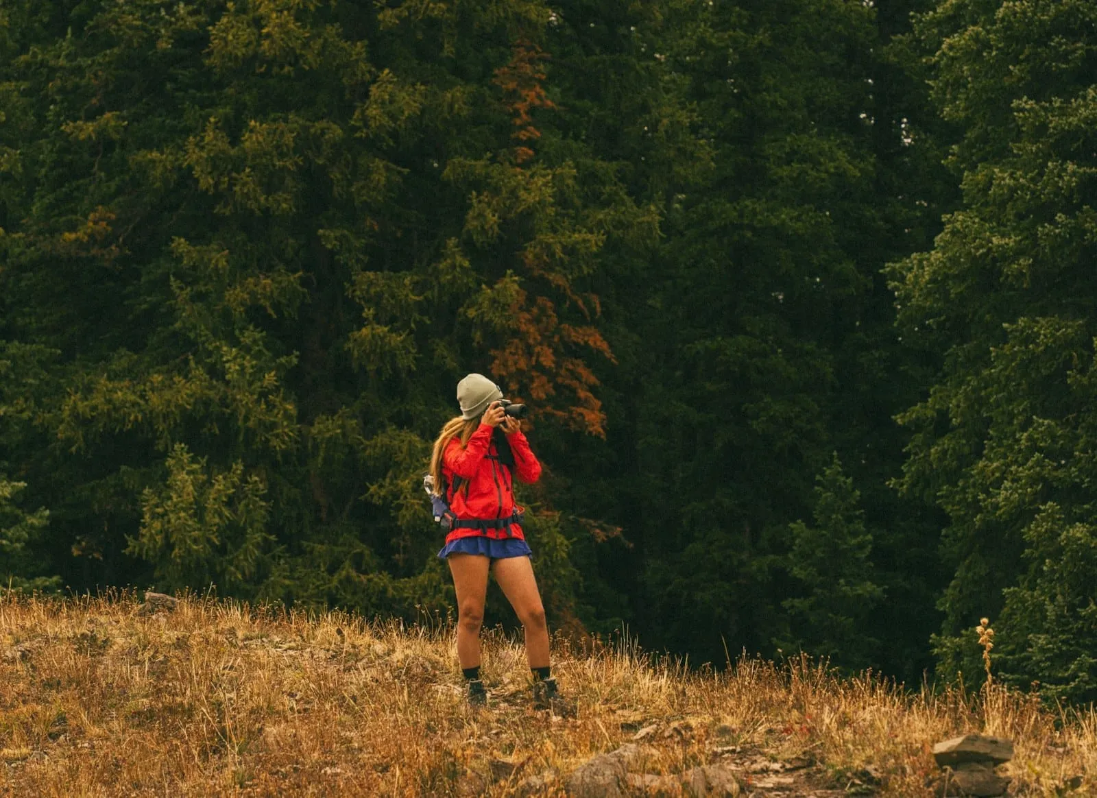 A trail runner drinking from a bottle on a grass track at the edge of a forest.