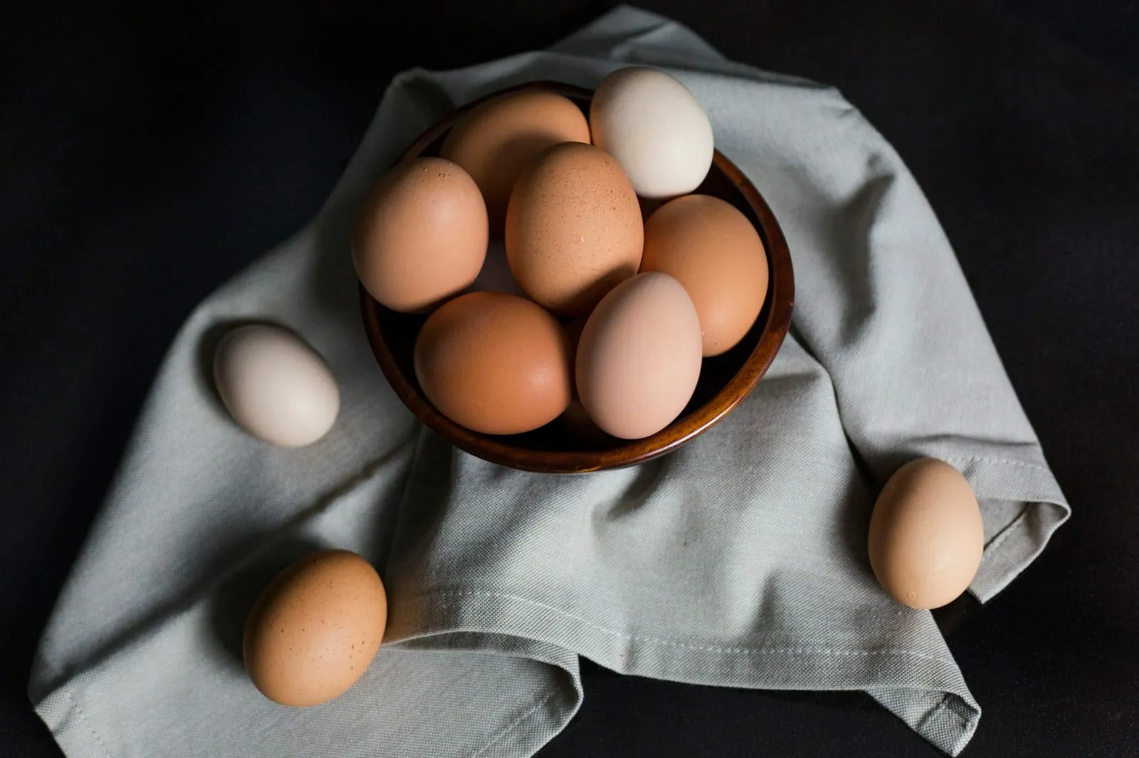 Brown and white eggs in a wooden bowl on grey linen.