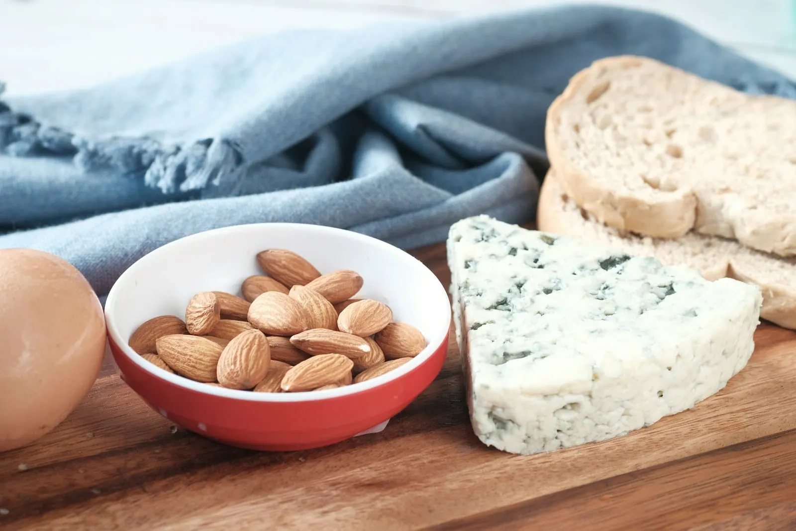 A bowl of almonds beside a wedge of blue cheese and sliced bread.