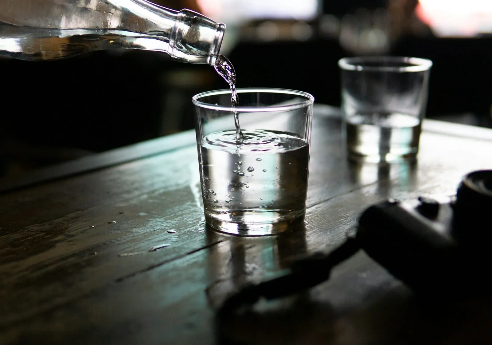 Water being poured into a glass on a dark wooden table.